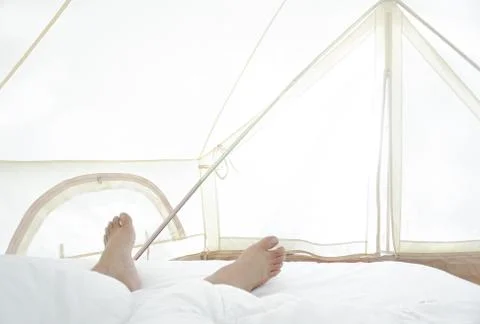 Close the barefoot man on the bed over the white blanket and sheets in the ho Stock Photos