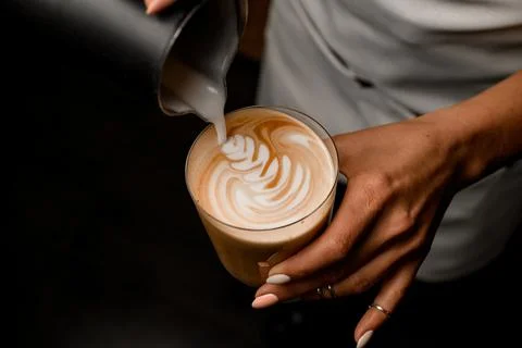 Close-up of barista gently drawing pattern pouring milk into glass with latte 스톡 사진