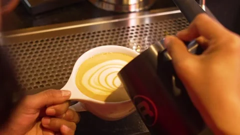Close-Up of Barista Hands Pouring Steamed Milk to Create Swirl Latte Art in Stock Footage 336401108