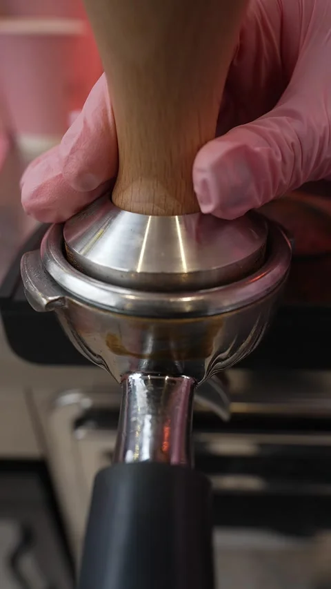 Close-up of a barista's hands using a tamper to press ground coffee into a Video stock 268490586