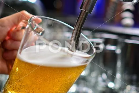 Close-up of barman hand at beer tap pouring a draught lager beer Stock Photos