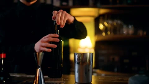 Close-up of a bartender in a dimly lit bar opening a bottle and preparing a Stock Footage 318648916