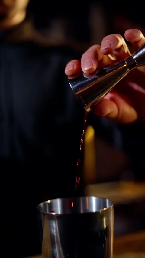 Close-up of a bartender measuring spirits with a metal jigger and pouring into a Video stock 318538294