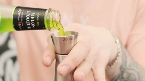 Close-up of a bartender pouring melon liqueur from a bottle into a jigger and th Vidéo 202233604