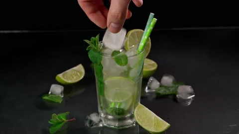A close-up of a bartender's Hand Putting Ice Cubes in a glass of Mojito Stock Footage 237436450