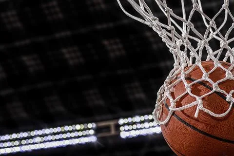 Close-up of a basketball falling through the net with arena lights in the Foto stock