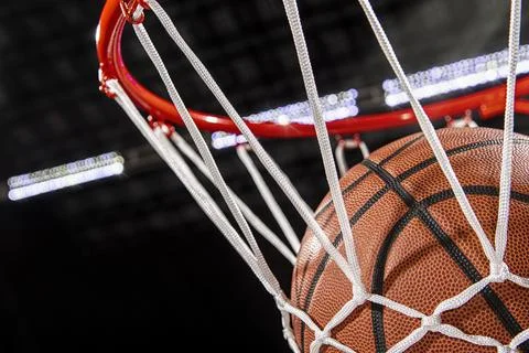 Close-up of a basketball falling through the net with arena lights in the Foto stock