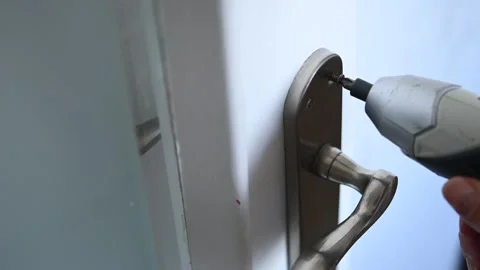 Close-up of a battery-powered cordless screwdriver screwing in a doorknob scr Stock Footage 320897651