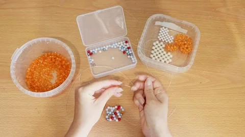 Close up of beadwork crafting hands stringing colorful beads on wooden tabl.. Video stock 339567798