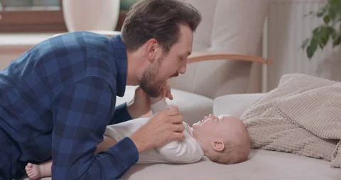 Close of bearded and mustashed father is kneeling by the baby lying on the couch Stockbeeldmateriaal 140171943