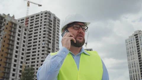 Close up of bearded engineer in hard hat talking on phone at construction site Video stock 346815043