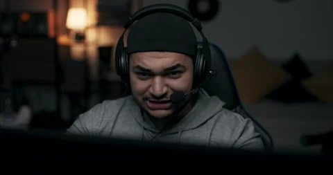 Close-up of bearded guy in cap wearing headphones. Man plays online game, he is Stock Footage 214633834