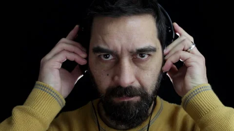 Close-up, a bearded man on a black background puts headphones to his ears Stock Footage 145400092