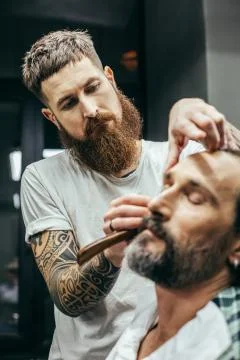 Close up of bearded man cutting beard of his client Stock Photos