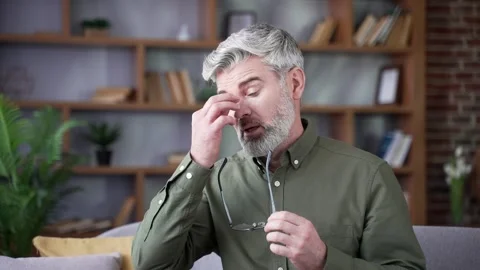 Close-up of bearded man with gray hair rubbing the bridge of his nose after  Stock Footage 328706180
