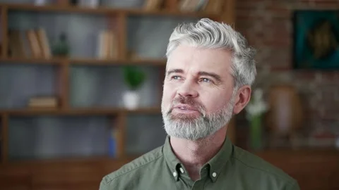 Close-up of bearded man with gray hair sitting on sofa at home, smiling and look Stock Footage 328706551