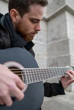 Close-up of a bearded man learning to play the guitar alone in an empty squar Stock Photos