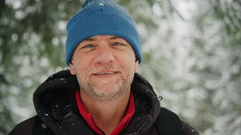 Close up of a bearded man smiling in a snowy forest wearing a blue beanie and Vídeos de archivo 342511328