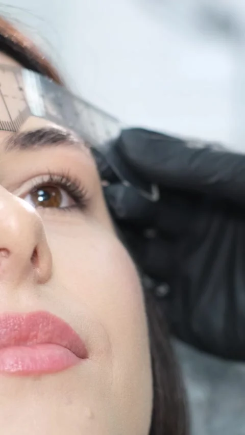 A close-up beautician corrects the shape of the eyebrows with a special ruler Stock Footage 250439793