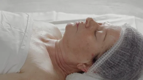 Close-up, beautician's hand applying rejuvenating cream to elderly woman's face Stock Footage 337123651