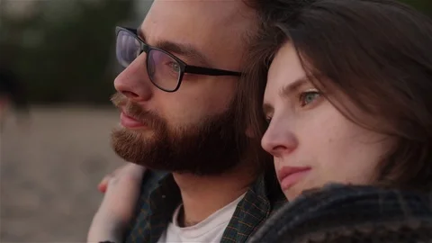 Close-up of beautiful sad couple sitting and hugging on the beach outside Stock Footage 110796562