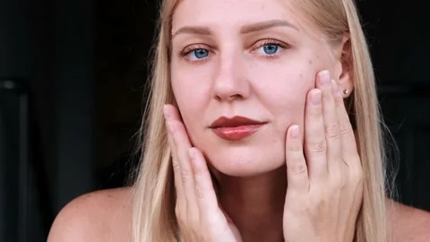 Close-up of beautiful woman's face. Young blue-eyed blonde girl touches her face 動画素材 216855262