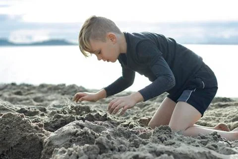A close up of a beautiful young boy playing in the sand on the beach. Stock Photos