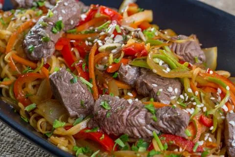 Close up of beef cuts, vegetables and spaghetti on a black plate Stock Photos
