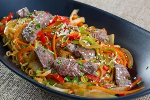 Close up of beef cuts, vegetables and spaghetti on a black plate Stock Photos