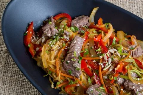 Close up of beef cuts, vegetables and spaghetti on a black plate Stock Photos