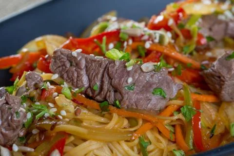Close up of beef cuts, vegetables and spaghetti on a black plate Stock Photos