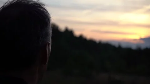 Close-up from behind of an man looks thoughtfully at the summer sunset Stock Footage 139676391