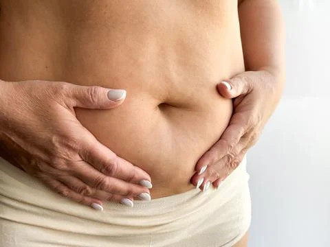 Close up of belly with hands gently touching in beige underwear on white Stock Photos