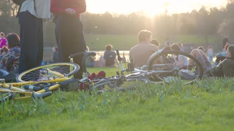 Close Up Of Bicycles Lying On Green Grass With Young People Relaxing Near A Stockbeeldmateriaal 331301171