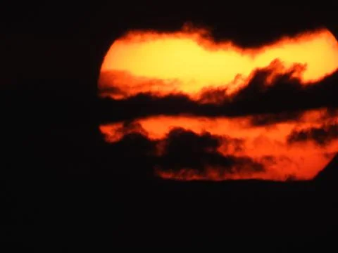 Close up of a big, yellow, setting sun in a red sky over the mountains of Ko Stock Photos