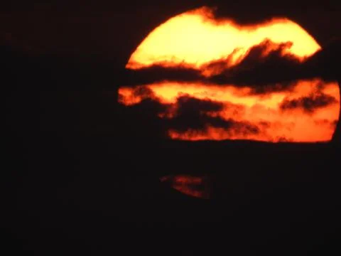 Close up of a big, yellow, setting sun in a red sky over the mountains of Ko Stock Photos