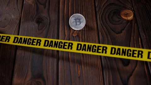 A close-up of a bitcoin coin and a yellow warning tape reading DANGER. Stock Footage 329277735
