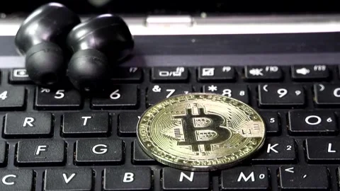 A close-up of a Bitcoin coin falling onto a black laptop keyboard Stock Footage 342256731
