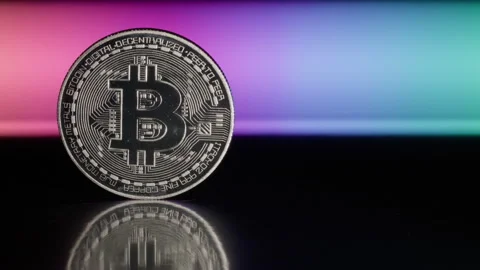 Close-up of a Bitcoin on a reflective surface with colorful background Stock Footage 328274280