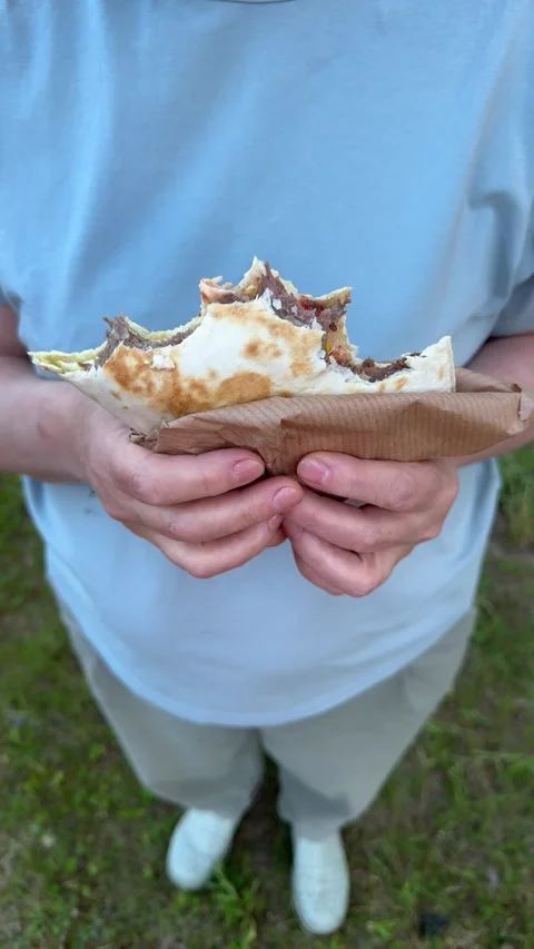 Close-up of bitten piece of shawarma in woman's hands outdoors, street food Vídeo Stock 338035956