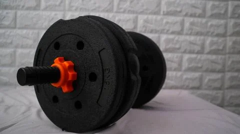 A close-up of a black adjustable dumbbell with orange accents, placed on a .. Stock Photos