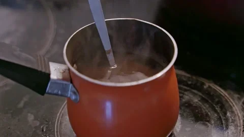 Close-up black arabica coffee brewed in orange turk standing on induction hob at Stock Footage 201326992
