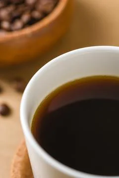 Close-up black beverage in white ceramic cup with softly blurred roasted bean Stock Photos
