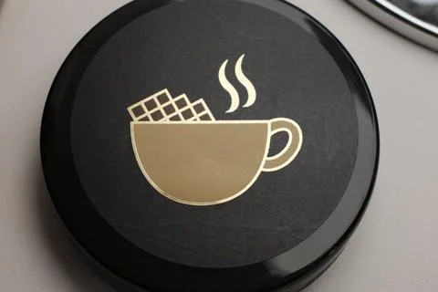 Close up on a black circular lid displaying a golden graphic of a hot drink. Fotos de archivo