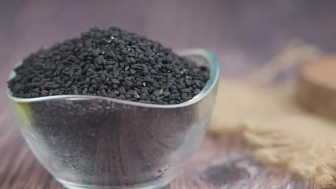 Close up of black cumin seeds in glass bowl with oil bottle cinematic motion. Video stock 331900290