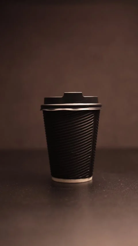 Close-up of a black disposable coffee cup with a ribbed texture against a dark Stock Footage 338432533