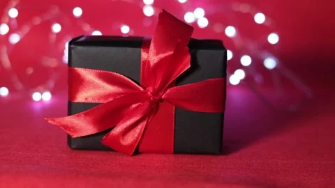 Close-up of a black gift box with a red bow on a red background. Stock Footage 165866511