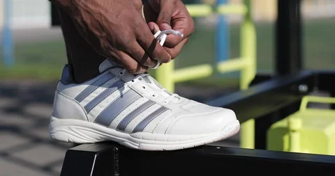 Close up of black hands of a man tying shoelaces in white crass. Stock Footage 102026371