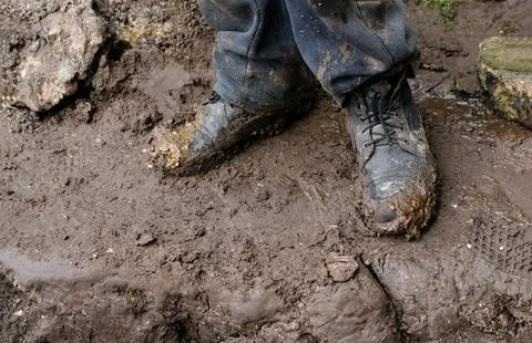 Close-up of black leather work boots covered in thick brown mud. Worker sta.. Fotos de archivo