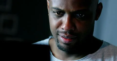 Close-up black man face looking at computer screen at night Stockfoto's